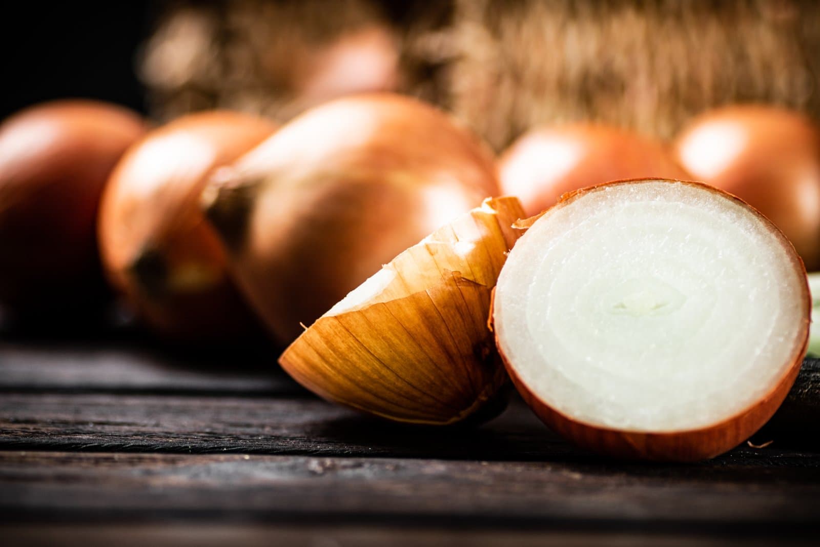 A whole brown onion, curled outer skin and a cut half showing the flesh